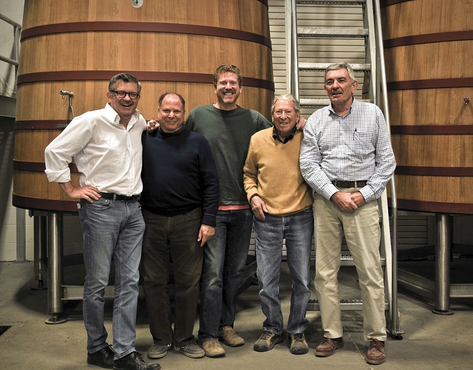 five men in front of large wooden wine tanks