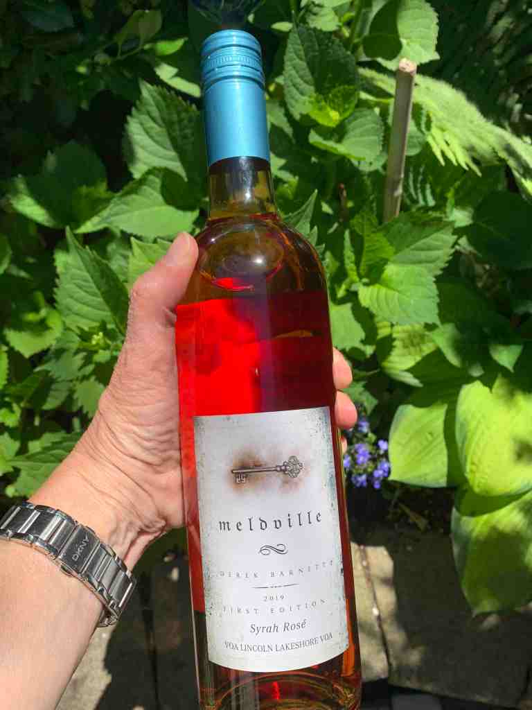 Bottle of Meldville Rose wine that's a bright pink in garden